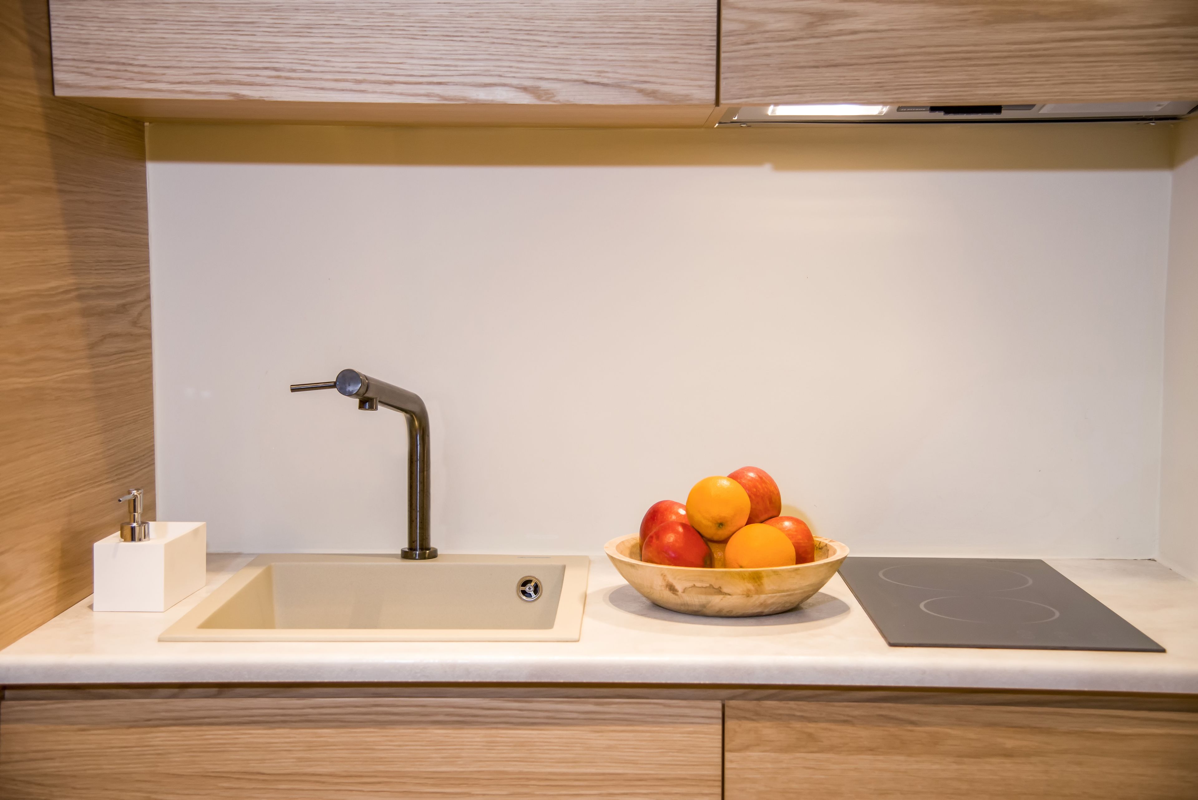 A modern kitchen with a sink, a bowl of fruit, and a built-in induction cooktop.
