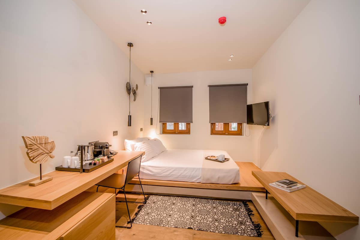 A compact bedroom with a single bed, a desk, and a TV mounted on the wall.