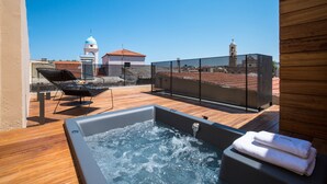 A rooftop terrace with a hot tub, lounge chairs, and a view of a church with a bell tower.