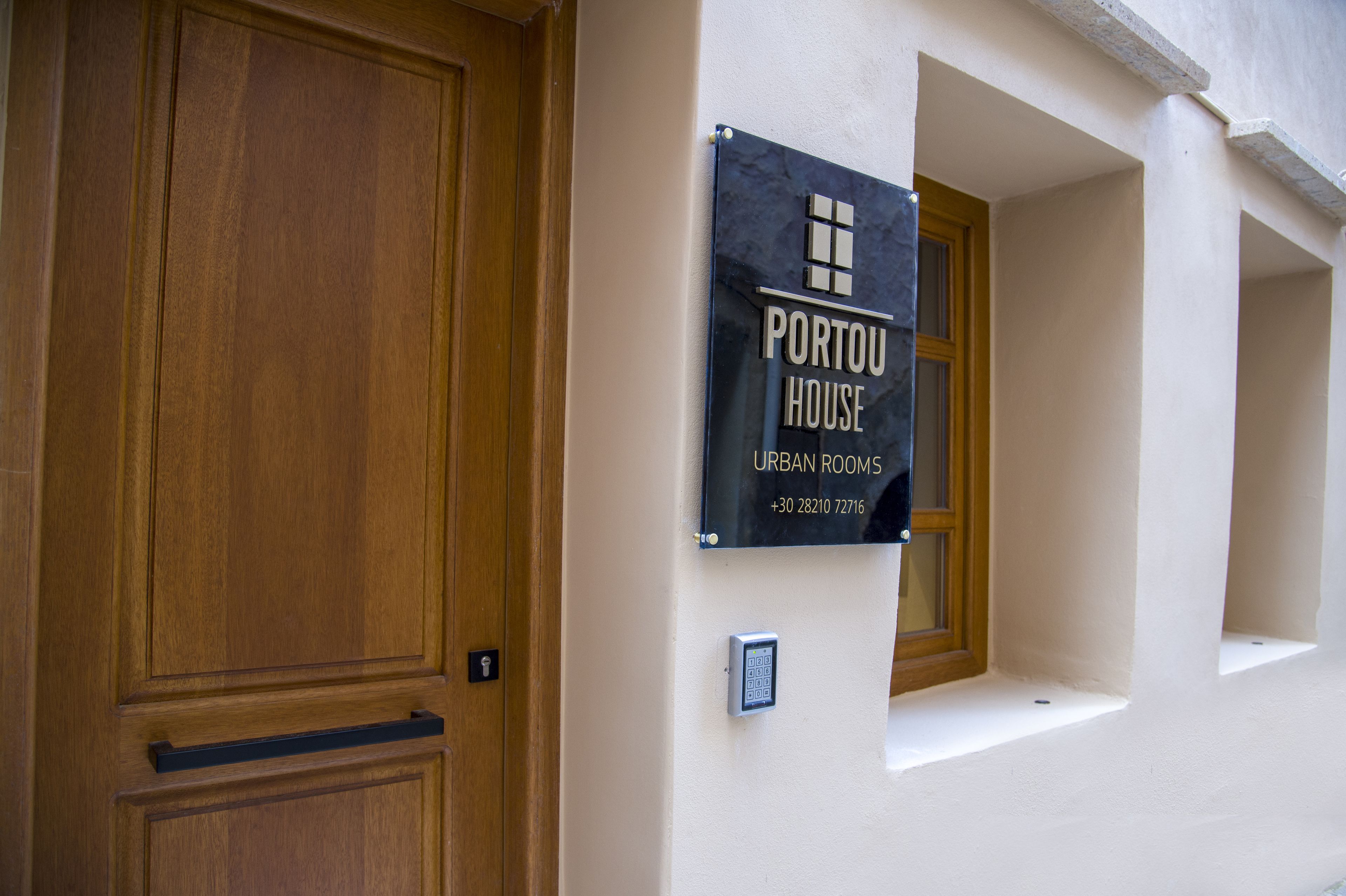 A wooden door and a sign for "Portou House Urban Rooms" with a contact number.