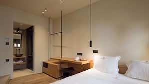 A modern hotel room with a wooden desk, a bed with white linens, and a minimalist design.