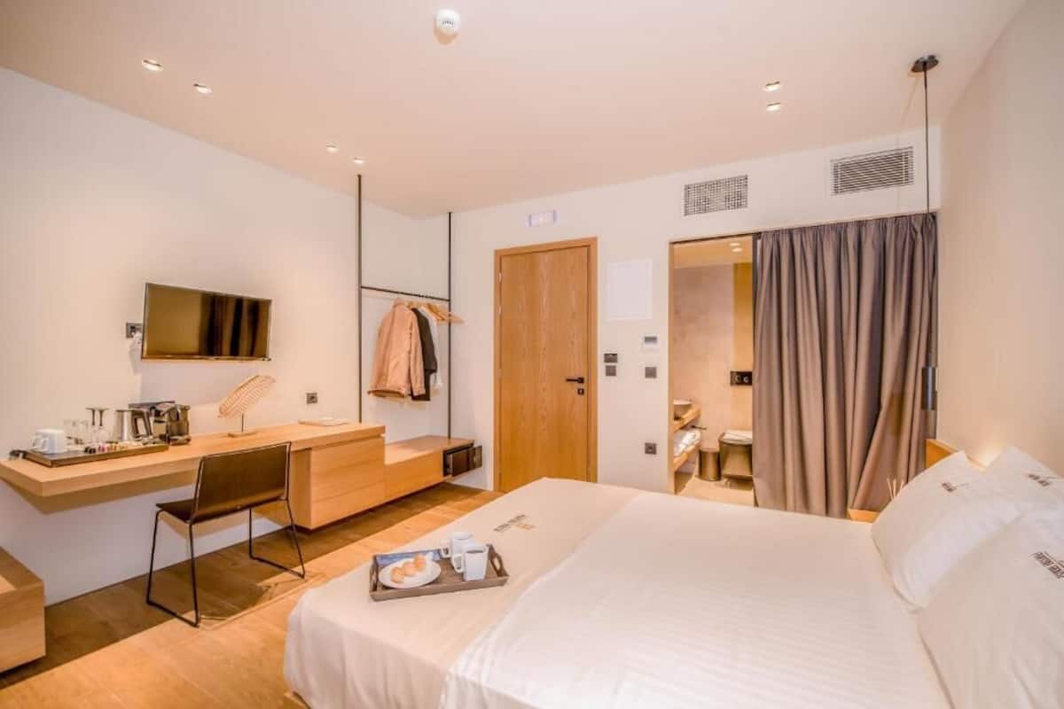 A modern hotel room with a bed, desk, chair, and a bathroom visible through an open door.