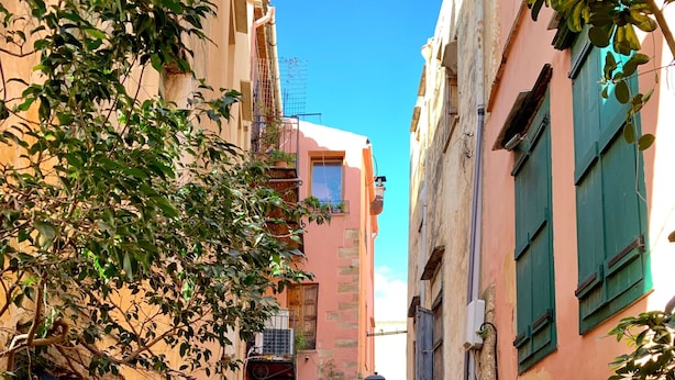 A narrow cobblestone street flanked by buildings with balconies and potted plants.