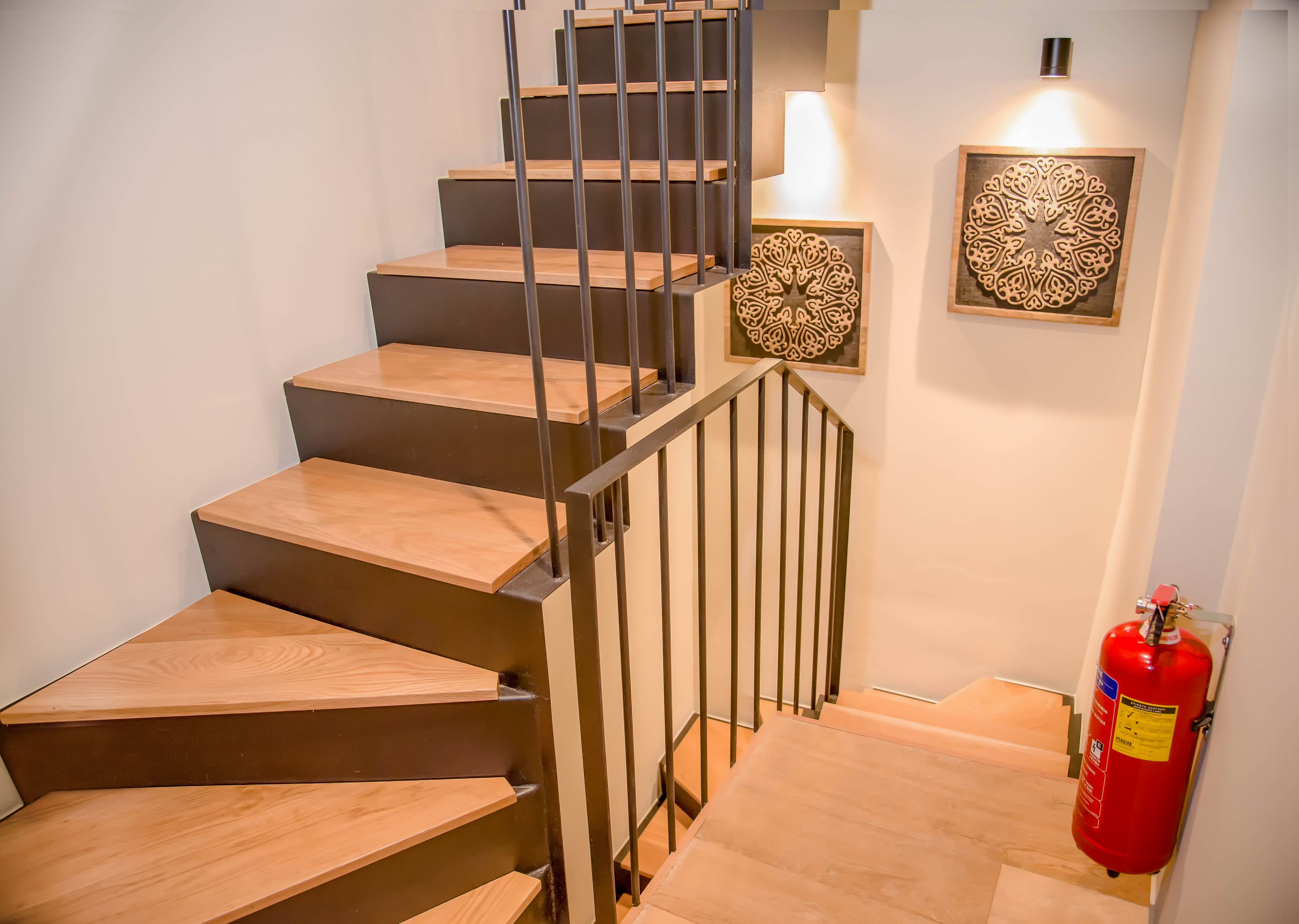 A staircase with wooden steps and metal railings, a wall-mounted fire extinguisher, and two decorative wall panels.
