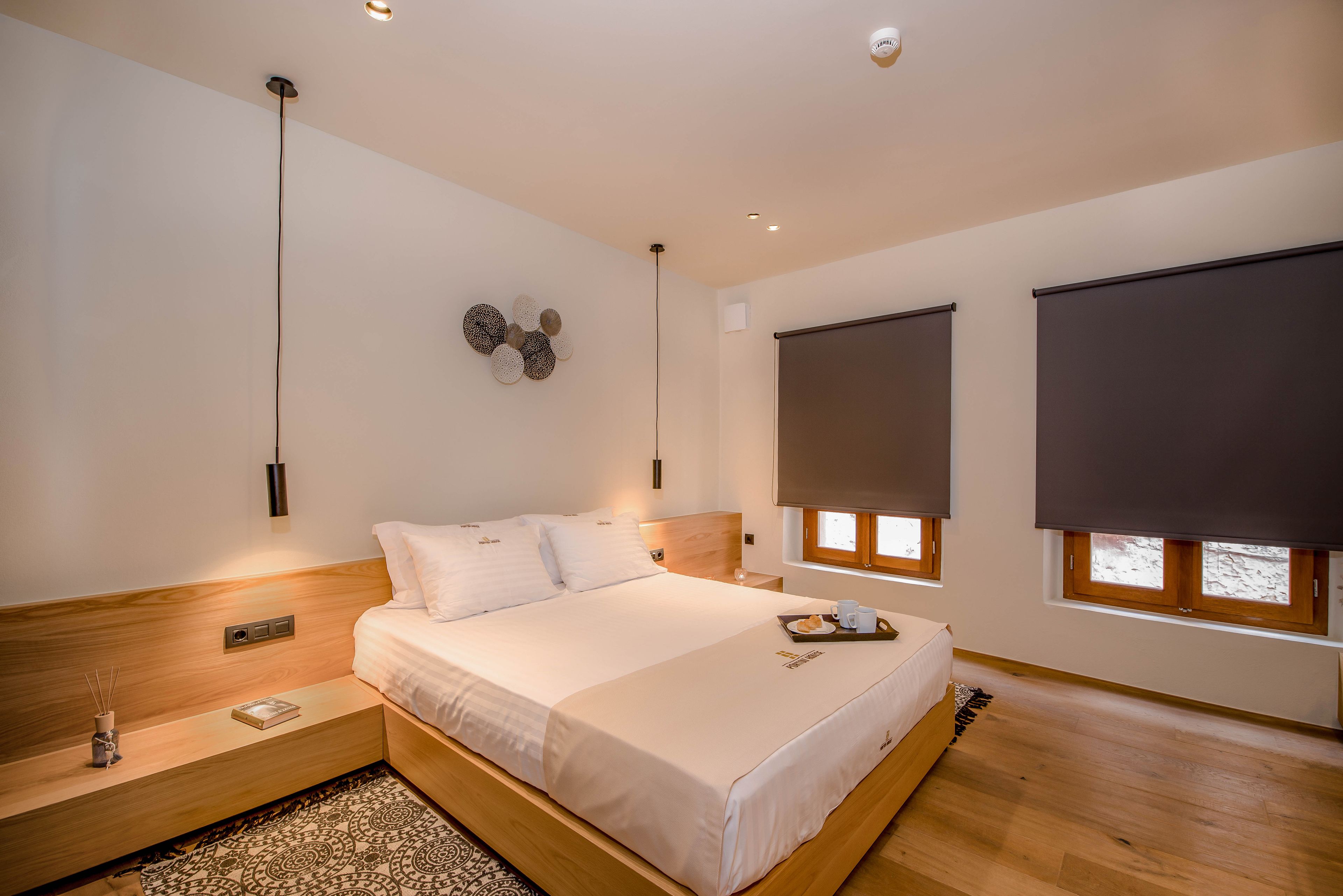 A modern bedroom with a large bed, a bedside table, a wall-mounted light, and a window with blinds.