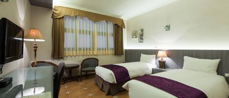 Habitación de hotel con dos camas, un escritorio, una silla, un televisor y una ventana con cortinas.