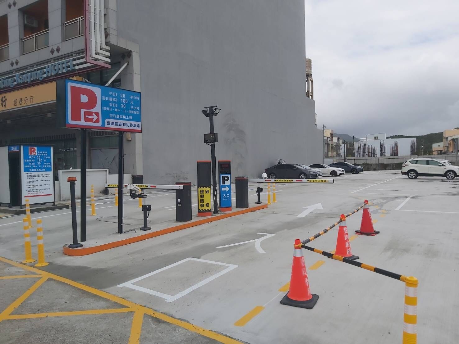 Un estacionamiento de hotel con un letrero azul de estacionamiento, una entrada con portón y varios coches aparcados.