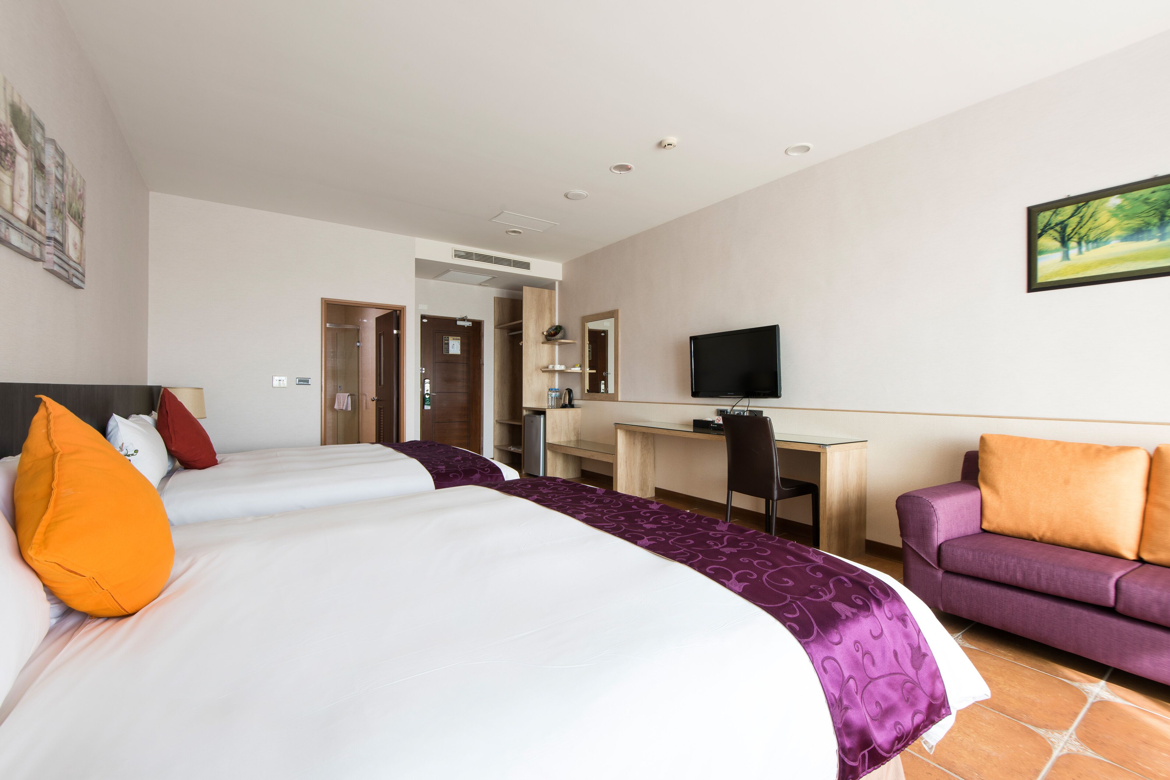 A hotel room with two beds, a desk, a TV, and a sofa.