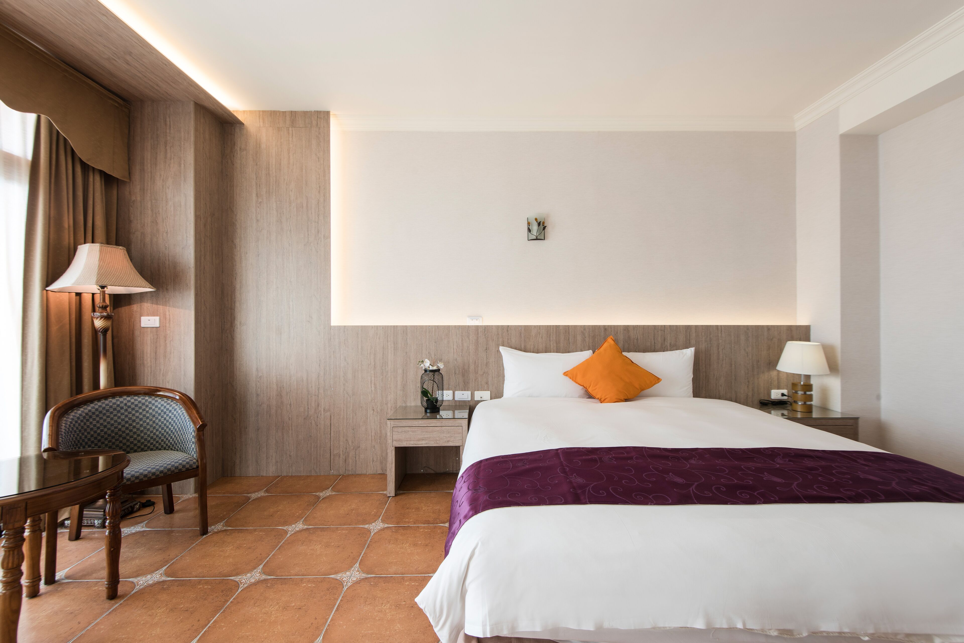 Ein Hotelzimmer mit einem großen Bett, einem Nachttisch, einem Sessel und einer Lampe.