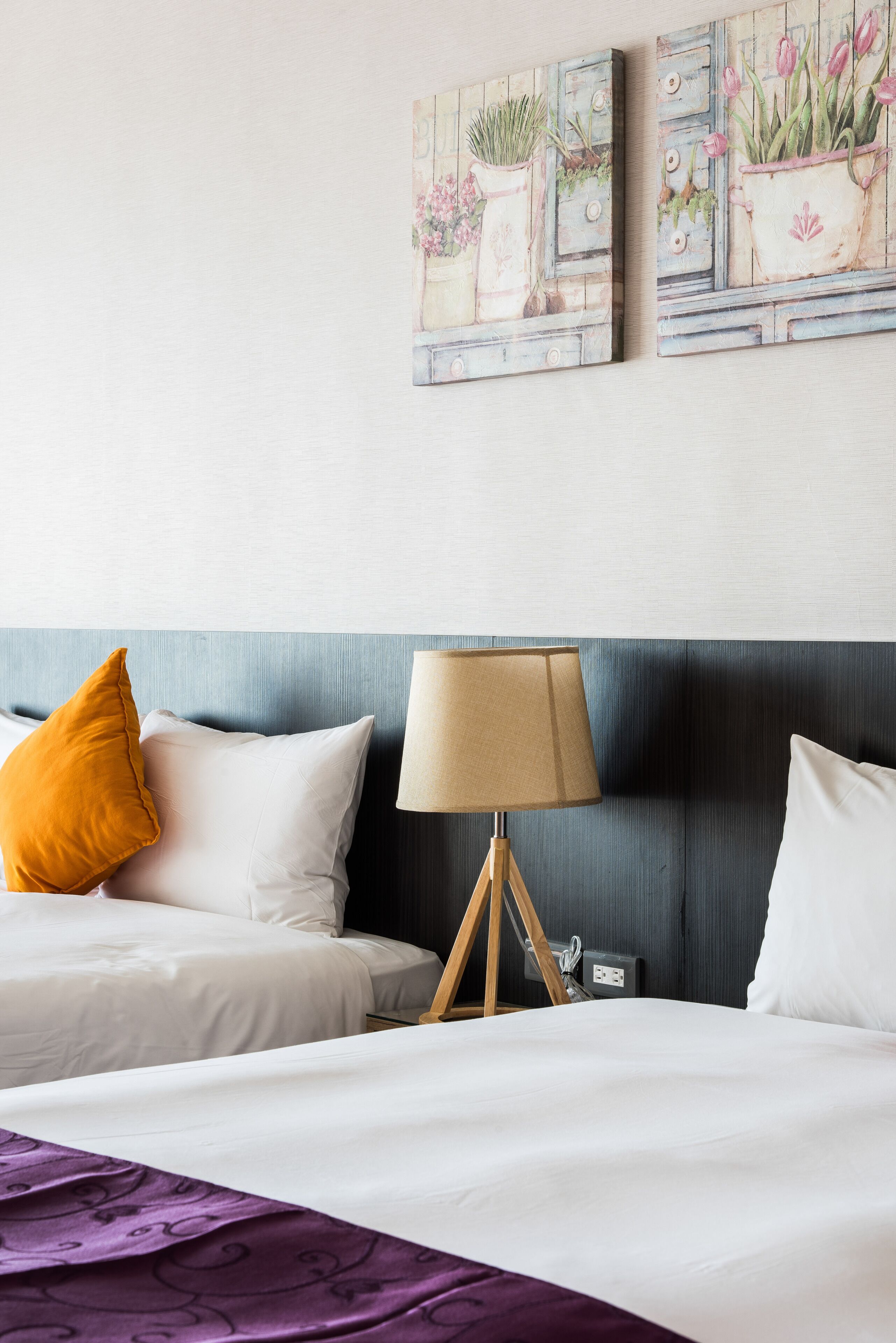 A hotel room with a bed, a lamp, and two paintings on the wall.