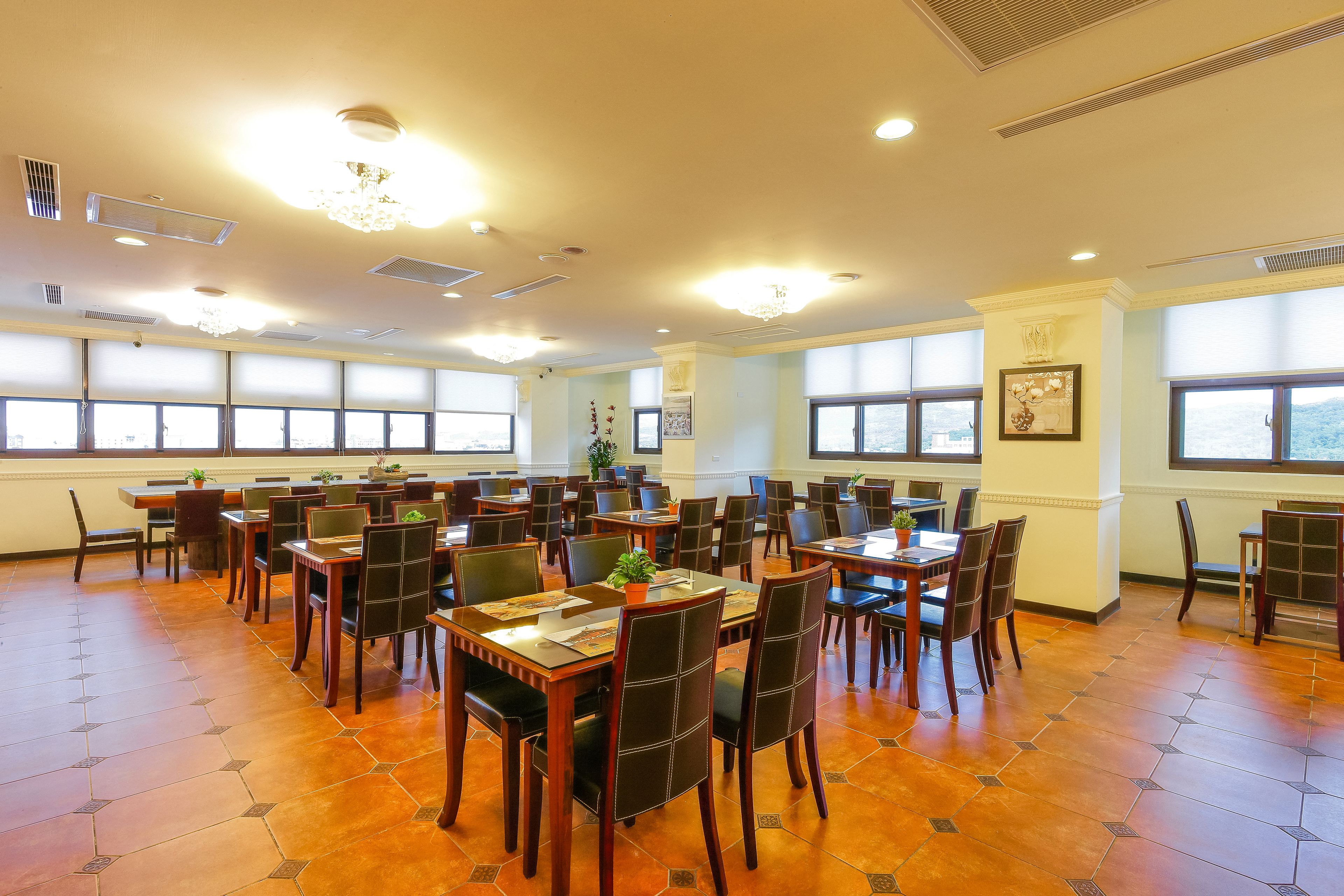Un comedor espacioso con varias mesas y sillas, ventanas amplias y piso de baldosas.