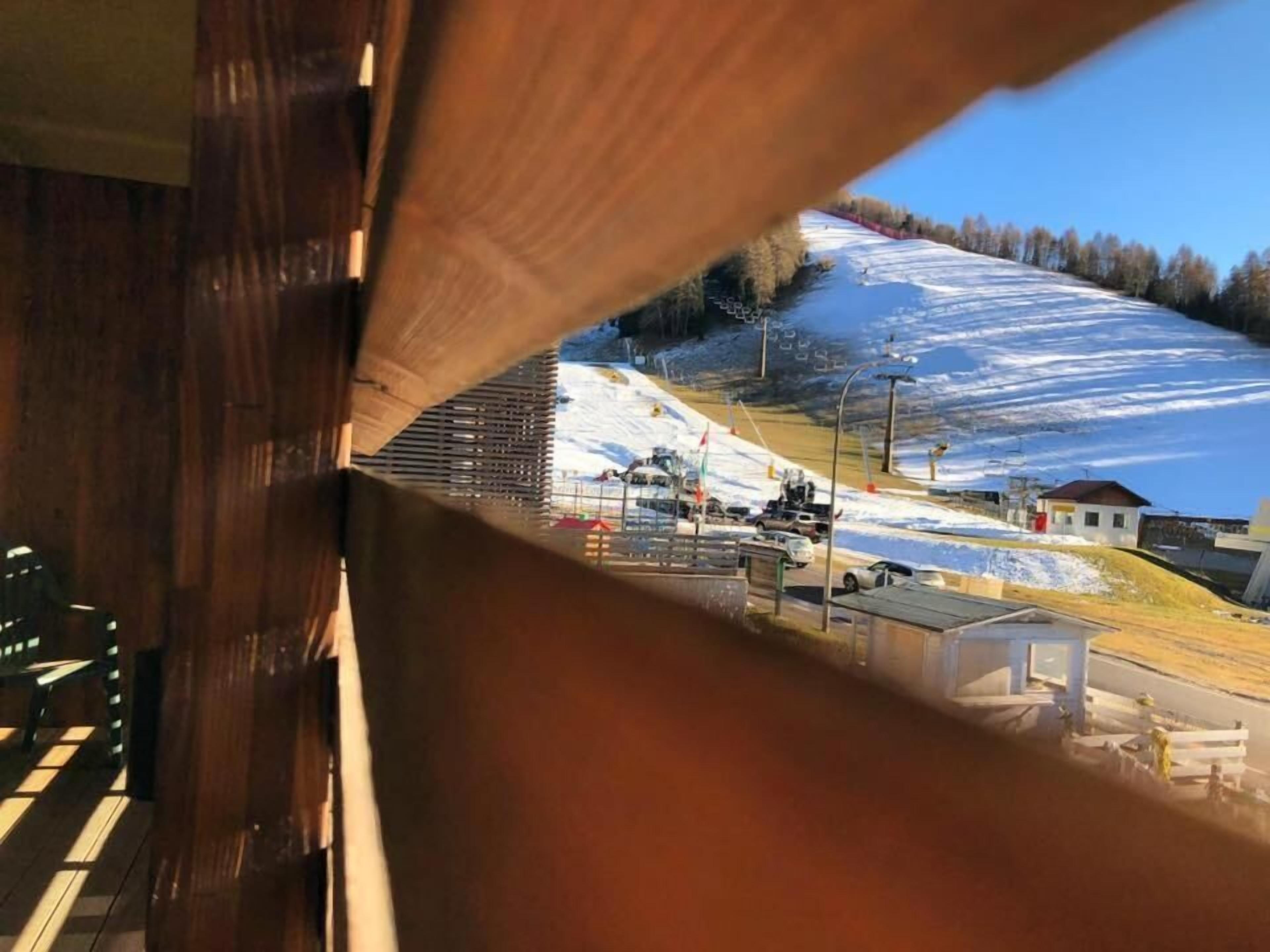 A view through a wooden structure with a snowy landscape, a road, and a small building in the distance.