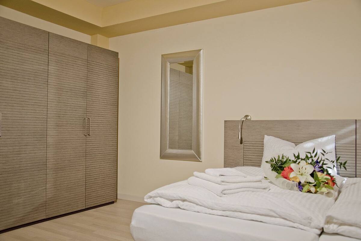 A bedroom with a large wardrobe, a bed with white linens, and a mirror on the wall.