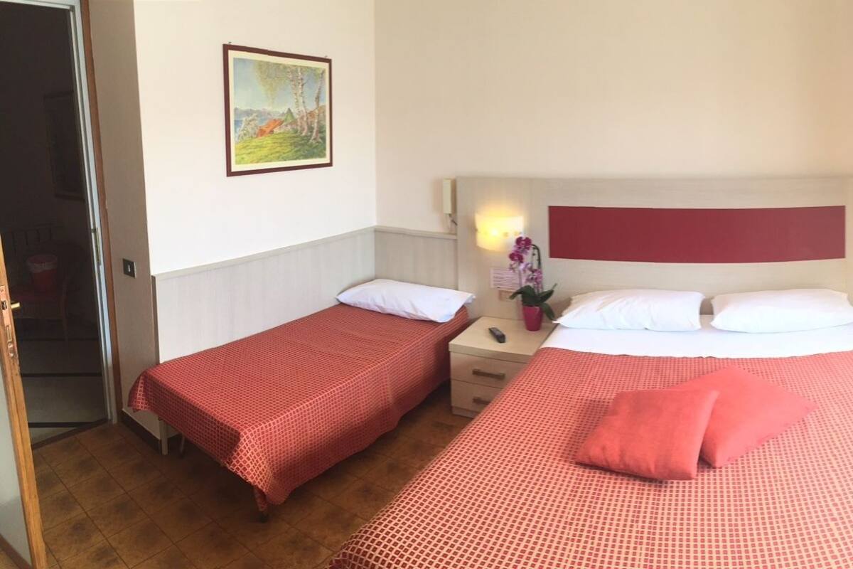 Habitación de hotel con dos camas individuales, una mesita de noche, una lámpara, un cuadro en la pared y una puerta al balcón.