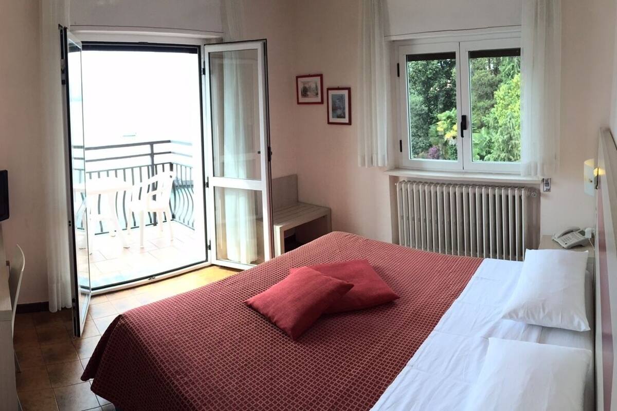 Habitación de hotel con cama, televisión, una mesita, una silla, ventana y balcón.