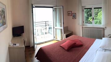 Ein Hotelzimmer mit Bett, Fernseher, kleinem Tisch, Stuhl, Fenster und Balkon.