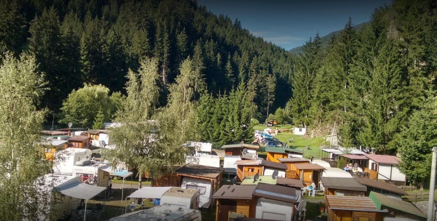 Ein Campingplatz mit Wohnmobilen und Holzhütten, umgeben von dichtem Wald.