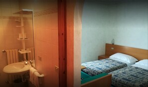 A bathroom with a sink, mirror, and towel rack. There is a wooden door leading to a bedroom with two beds and a nightstand. - Camping Hotel La Pineta (Valdidentro)
