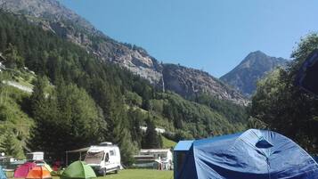 A campsite with tents and RVs, surrounded by mountains and trees.