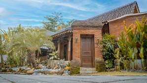 A traditional brick building with a wooden door, surrounded by tropical plants and a stone pathway.