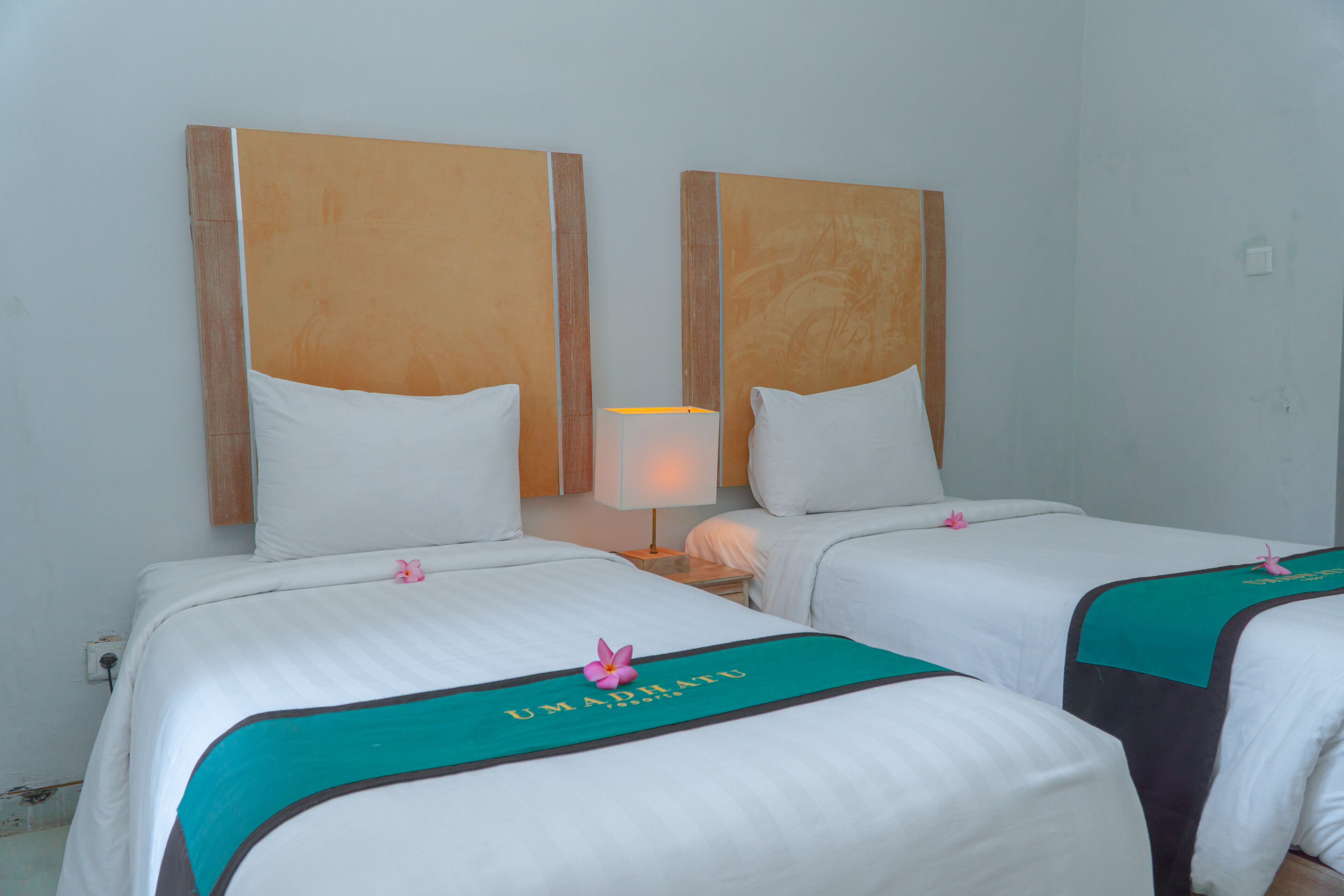 A hotel room with two beds, each with a teal bedspread and a pink flower decoration.