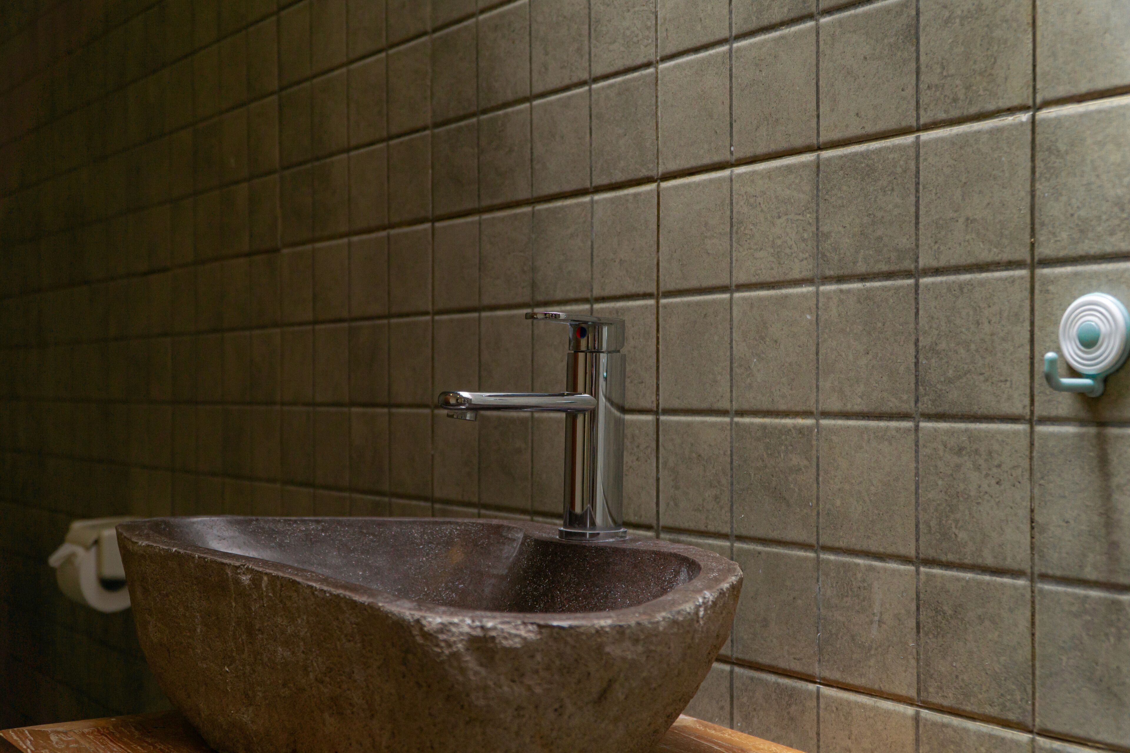Ein Waschbecken aus Stein mit einem modernen Wasserhahn in einem Badezimmer mit Fliesenwänden.