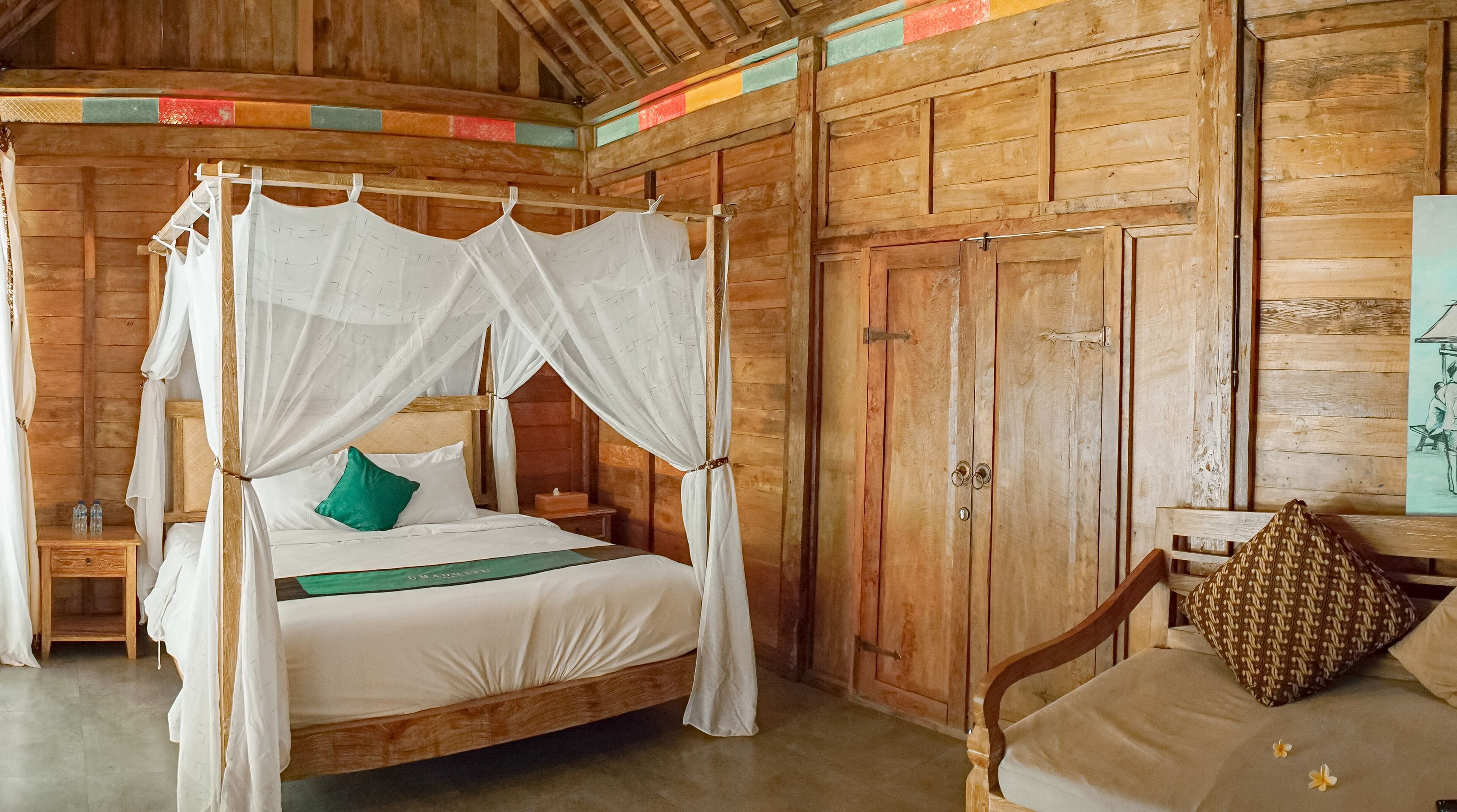 A wooden four-poster bed with a canopy, a green pillow, and a wooden nightstand with bottles.