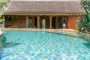 Ein Schwimmbecken mit Fliesenboden und ein Gebäude mit einem geflasten Dach im Hintergrund.
