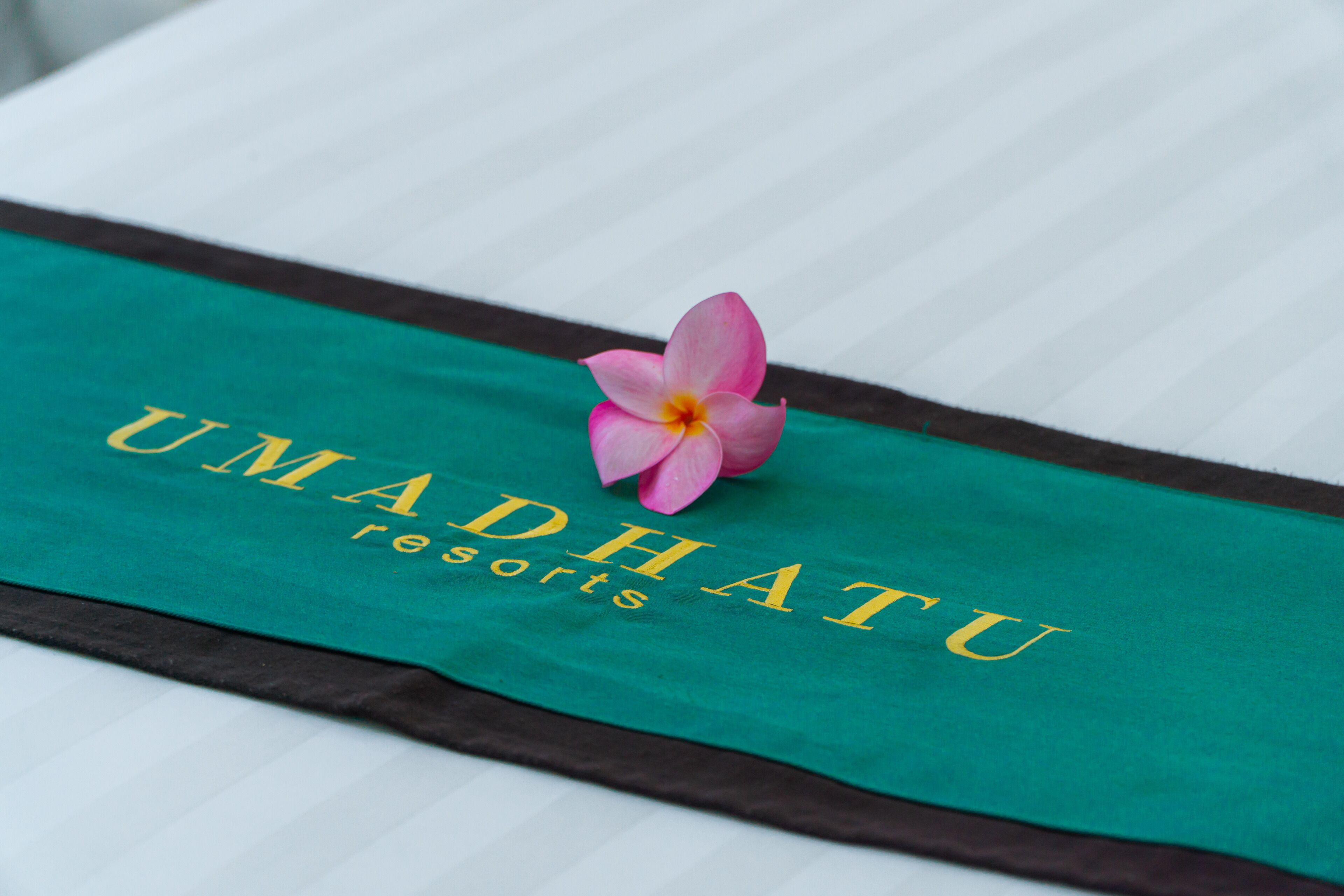 A bed with a green and brown bedspread featuring the text "UMADHATU resorts".