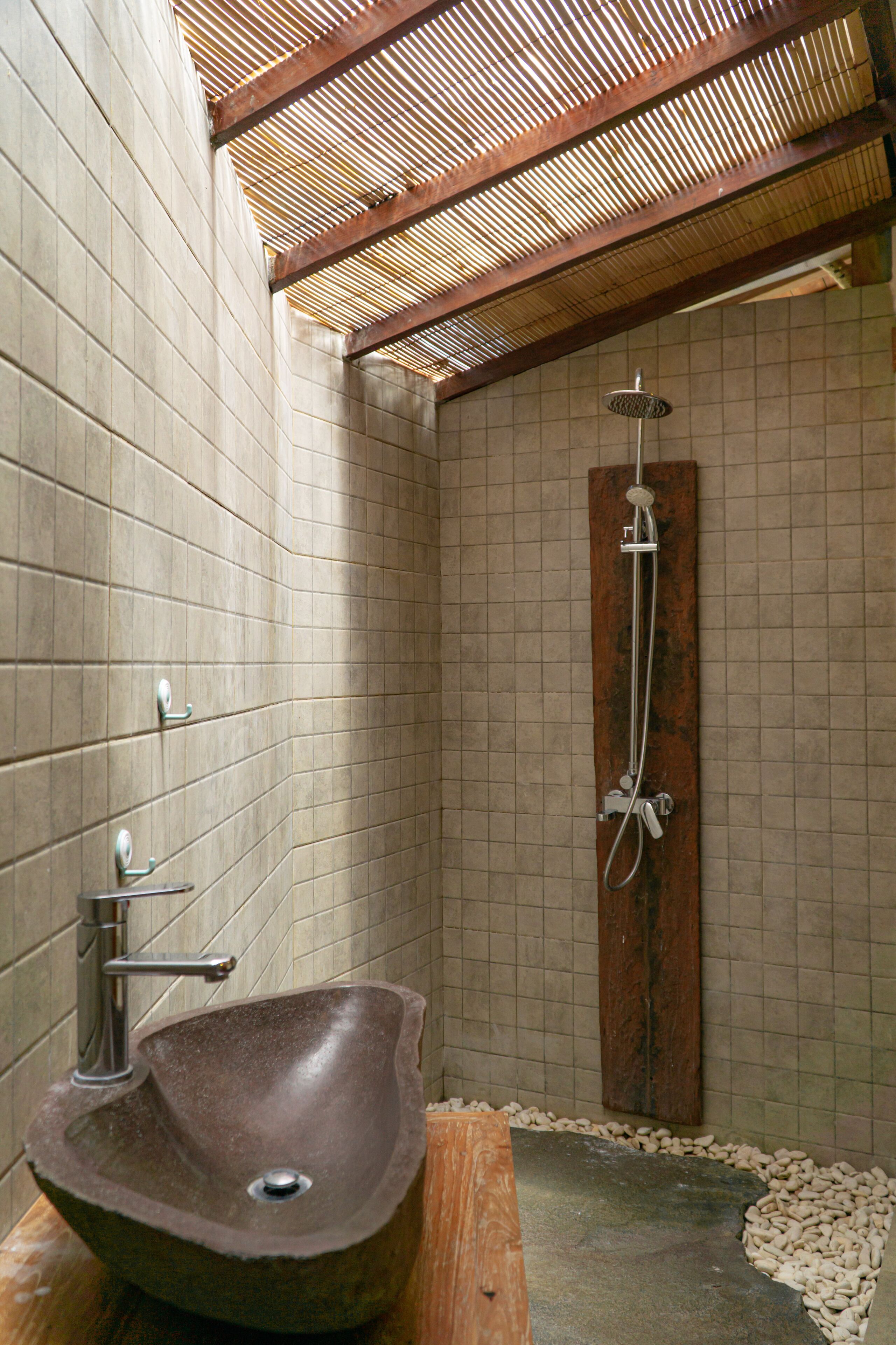 A bathroom with a stone sink, a shower, and tiled walls.