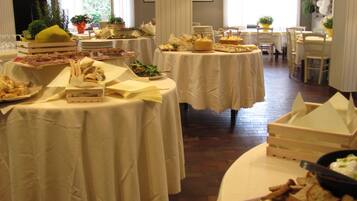 A dining area with multiple round tables covered with white tablecloths, each set with plates, cutlery, and various food items.