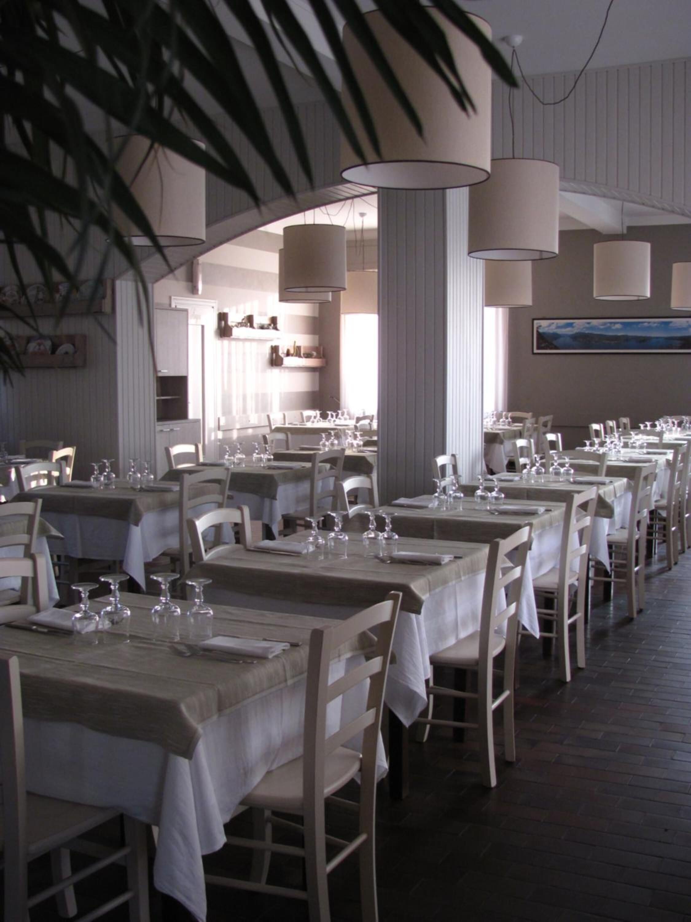 A restaurant with multiple tables set for dining, featuring white tablecloths and chairs, and large hanging lamps.