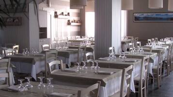 A restaurant with multiple tables set for dining, featuring white tablecloths and chairs, and large hanging lamps.