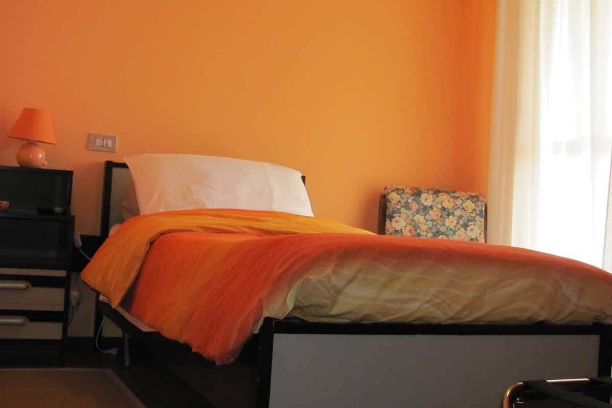 A bedroom with a bed, a nightstand, a lamp, and a floral-patterned picture frame.
