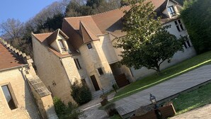 A historic building with a stone facade, a tiled roof, and a paved courtyard with benches and planters. - Auberge du jeu darc (Mello)