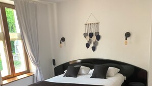A bedroom with a large bed, a bench, a bedside table, and a wall-mounted light fixture. - Auberge du jeu darc (Mello)