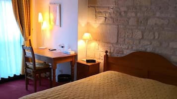A hotel room with a bed, a desk, two lamps, a chair, and a stone wall.