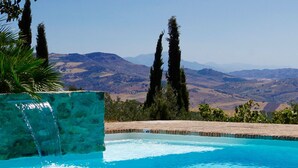 Une piscine à l’eau d’un bleu cristallin, entourée d’un mur de pierre et offrant une vue sur des montagnes lointaines.