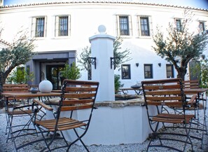 An outdoor seating area with wooden tables and chairs, a central fountain, and a white building with windows in the background. - La Posada del Torcal (Villanueva de la Concepcion)