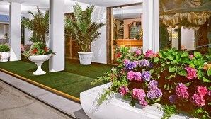 L’entrée d’un hôtel, avec une pelouse verdoyante, des plantes en pot et une porte vitrée donnant accès à l’intérieur.