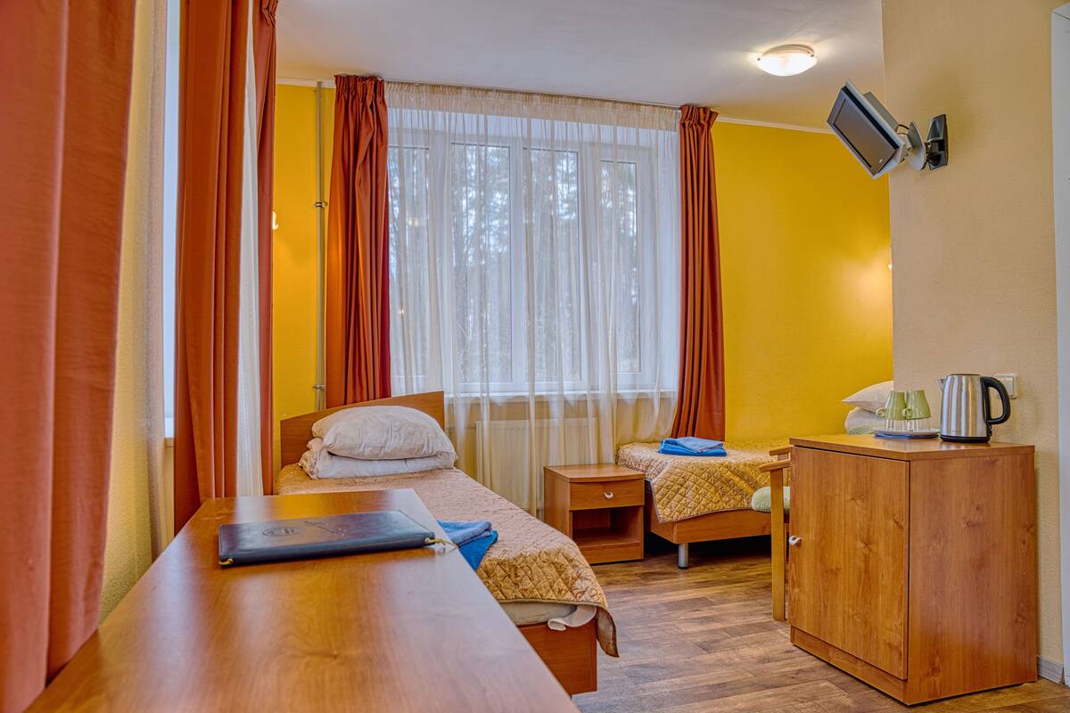 A room with two beds, a wooden desk, a small cabinet, and a television mounted on the wall.