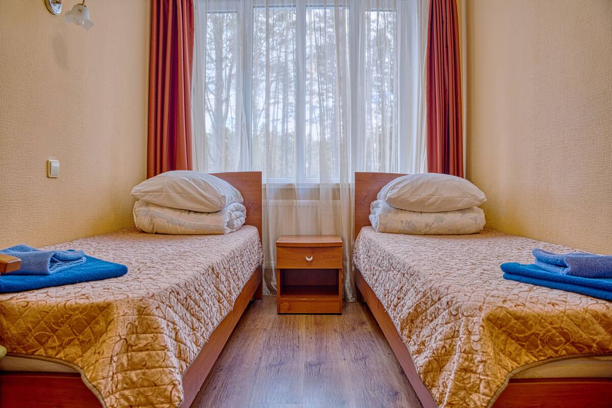 A hotel room with two beds, a nightstand, and a window with curtains.