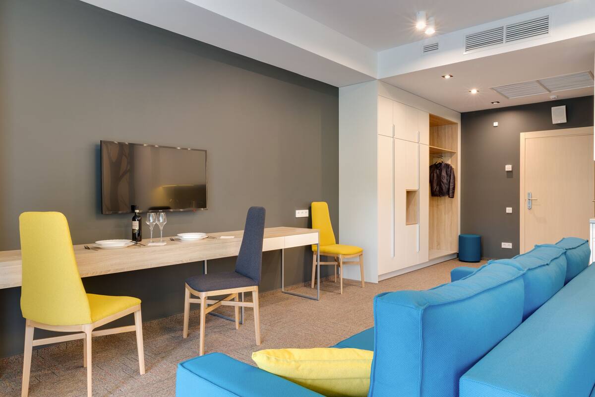 A modern hotel room with a dining area, a sofa, and a wardrobe.
