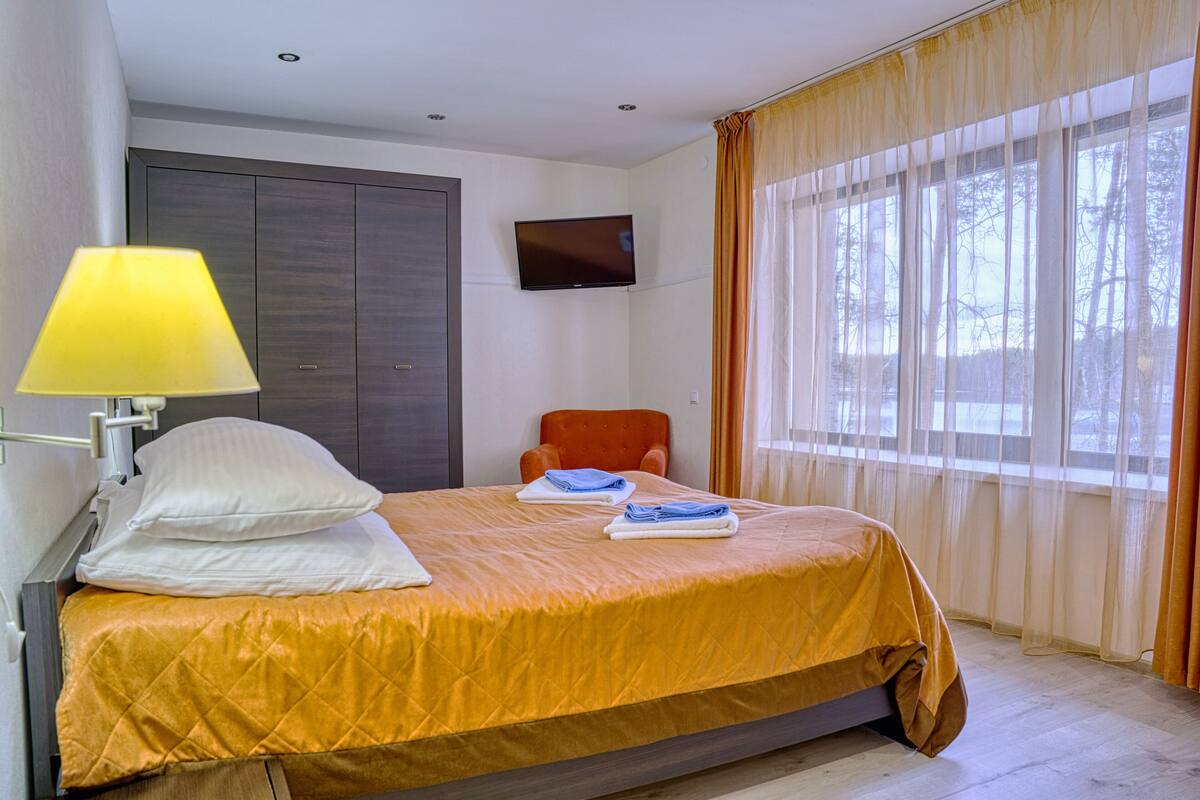 A hotel room with a bed, a TV mounted on the wall, a chair, and a window with curtains.