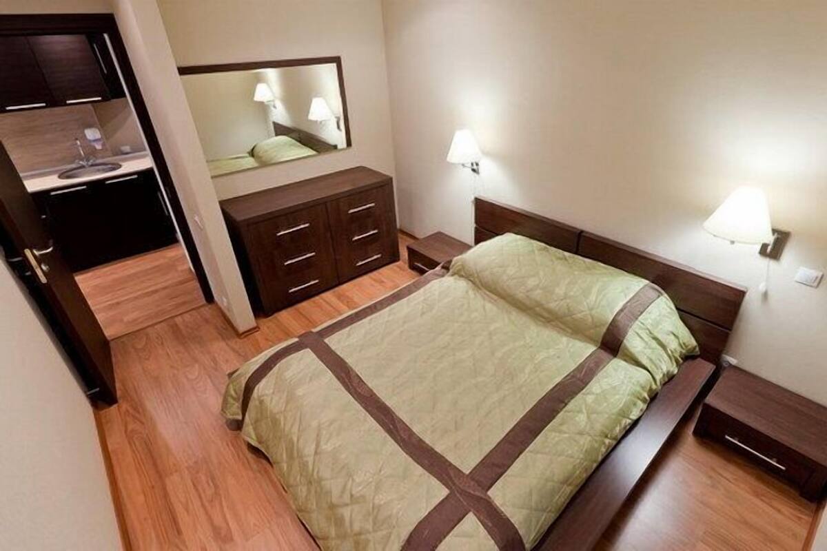 A bedroom with a bed, a dresser, a mirror, and two bedside lamps.