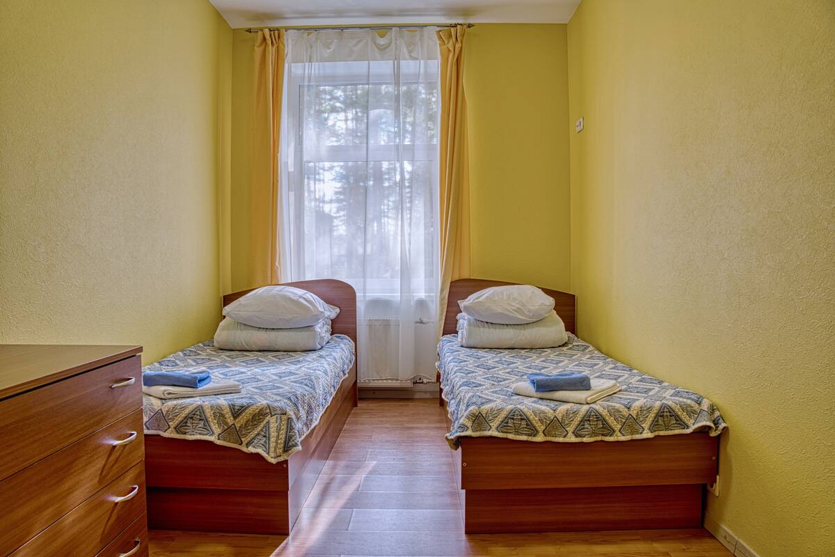 A room with two wooden beds, a wooden dresser, and a window with yellow curtains.