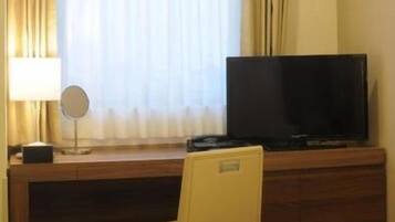 Una habitación de hotel con cama, escritorio con televisor, silla y ventana con cortinas.