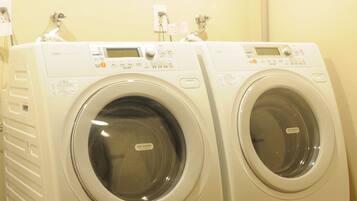 Two front-loading washing machines in a laundry room with a plain wall and a visible plumbing pipe.