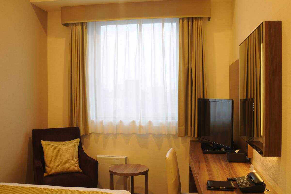 Une chambre d’hôtel avec un lit, un bureau avec une télévision, une chaise et une petite table.