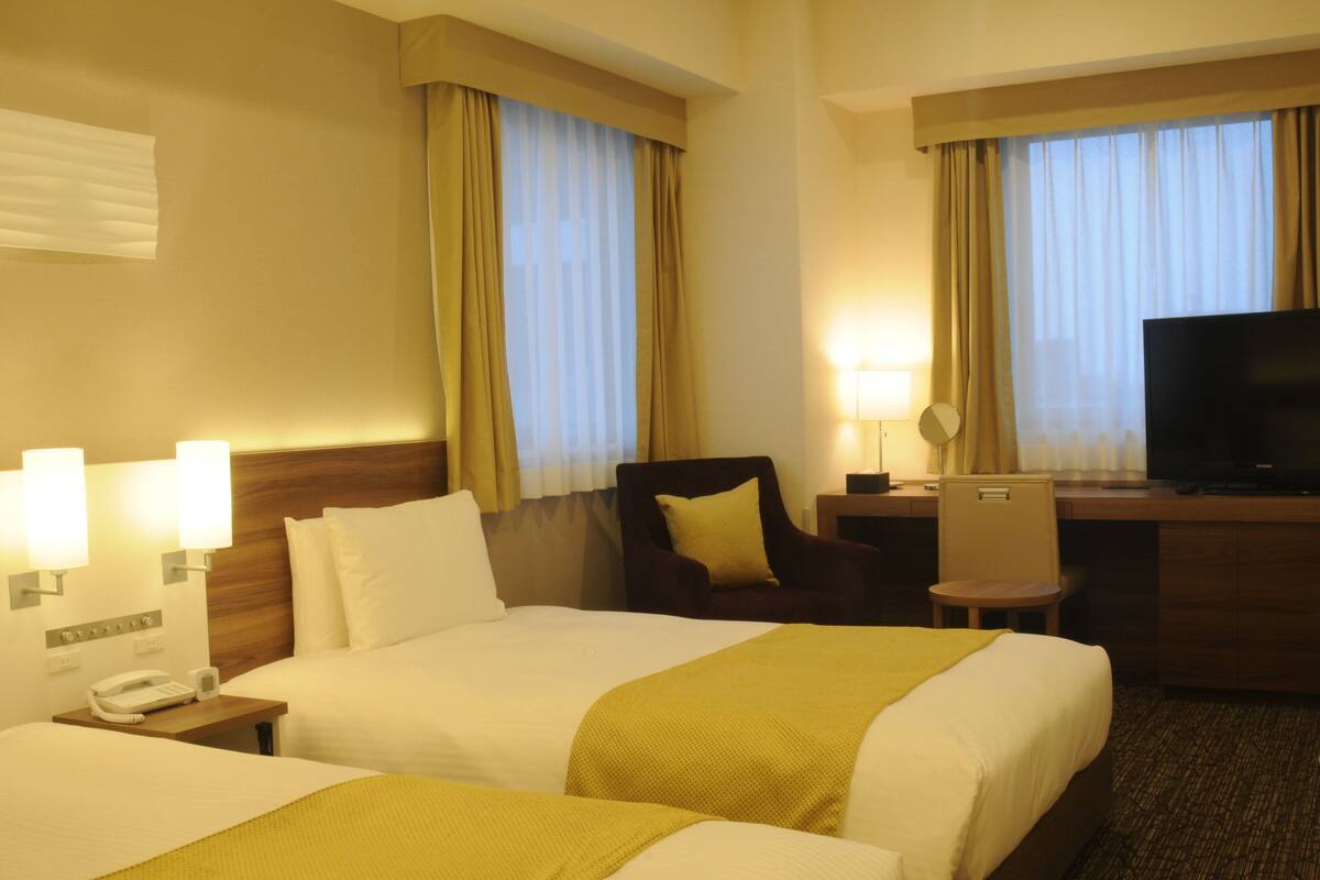 Une chambre d’hôtel avec deux lits, un bureau, une chaise, une télévision et un téléphone.